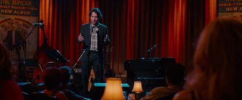 Movie still from “This Is 40” (2012), directed by Judd Apatow – A man standing in front of a microphone on a stage; Medium shot, Over the shoulder angle