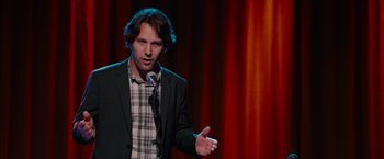 Movie still from “This Is 40” (2012), directed by Judd Apatow – A man standing on a stage holding a microphone; Medium shot, Over the shoulder angle