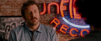 Movie still from “This Is 40” (2012), directed by Judd Apatow – A man standing in front of a neon sign in a room; Close Up shot, Over the shoulder angle