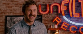 Movie still from “This Is 40” (2012), directed by Judd Apatow – A man with a beard and a tie in front of a neon sign; Close Up shot, Over the shoulder angle