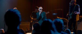 Movie still from “This Is 40” (2012), directed by Judd Apatow – A man in a green suit is singing; Wide shot, Over the shoulder angle