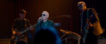 Movie still from “This Is 40” (2012), directed by Judd Apatow – An older man singing into a microphone on a stage; Medium shot, Over the shoulder angle