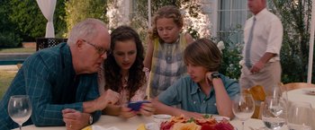 Movie still from “This Is 40” (2012), directed by Judd Apatow – A group of people sitting around a table looking at a cell phone; Medium shot, Over the shoulder angle