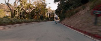 Movie still from “This Is 40” (2012), directed by Judd Apatow – A man riding a bike down a street with trees in the background; Extreme Wide shot, High angle