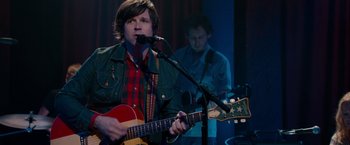 Movie still from “This Is 40” (2012), directed by Judd Apatow – A man playing a guitar while another man stands behind him; Medium shot, Over the shoulder angle