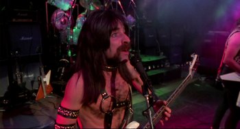 Movie still from “This Is Spinal Tap” (1984), directed by Rob Reiner – A man with long black hair is holding a guitar; Medium shot, Low angle