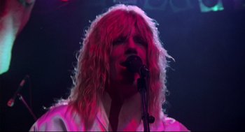 Movie still from “This Is Spinal Tap” (1984), directed by Rob Reiner – A person with long hair is singing into a microphone; Close Up shot, Low angle