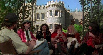 Movie still from “This Is Spinal Tap” (1984), directed by Rob Reiner – A group of people sitting in front of a castle; Wide shot, High angle