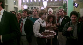 Movie still from “This Is Spinal Tap” (1984), directed by Rob Reiner – A group of people standing around a man holding a plate of food; Medium shot, Over the shoulder angle