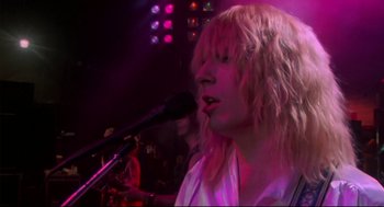 Movie still from “This Is Spinal Tap” (1984), directed by Rob Reiner – A person with long blonde hair singing into a microphone in front of a crowd; Close Up shot, Low angle