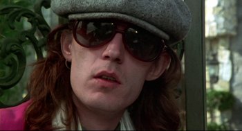 Movie still from “This Is Spinal Tap” (1984), directed by Rob Reiner – A person wearing sunglasses and a hat; Close Up shot, Low angle