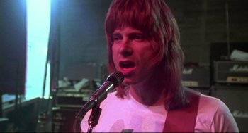 Movie still from “This Is Spinal Tap” (1984), directed by Rob Reiner – A man with long brown hair is singing into a microphone; Close Up shot, Low angle