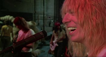 Movie still from “This Is Spinal Tap” (1984), directed by Rob Reiner – A person with a bottle of wine in their mouth; Close Up shot, Low angle