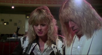 Movie still from “This Is Spinal Tap” (1984), directed by Rob Reiner – A woman and a man with blonde hair and a black and white shirt; Close Up shot, Low angle