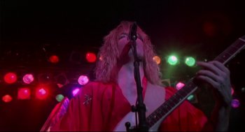 Movie still from “This Is Spinal Tap” (1984), directed by Rob Reiner – A person with a red jacket is playing a guitar; Medium shot, Low angle
