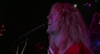Movie still from “This Is Spinal Tap” (1984), directed by Rob Reiner – A man with long blonde hair singing into a microphone; Close Up shot, Low angle
