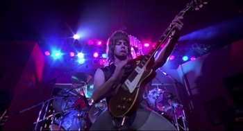 Movie still from “This Is Spinal Tap” (1984), directed by Rob Reiner – A man playing a guitar in front of a crowd; Medium shot, Low angle