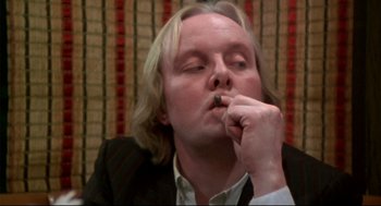 Movie still from “This Is Spinal Tap” (1984), directed by Rob Reiner – A man sitting in front of a wall smoking a cigarette; Close Up shot, Low angle