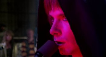 Movie still from “This Is Spinal Tap” (1984), directed by Rob Reiner – A person with a microphone in front of a purple background; Extreme Close Up shot, Over the shoulder angle