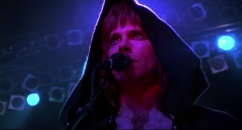 Movie still from “This Is Spinal Tap” (1984), directed by Rob Reiner – A man with a microphone wearing a black hooded robe; Close Up shot, Low angle