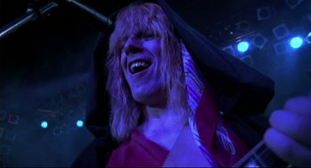 Movie still from “This Is Spinal Tap” (1984), directed by Rob Reiner – A man with long blonde hair wearing a purple tie; Close Up shot, Low angle