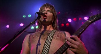 Movie still from “This Is Spinal Tap” (1984), directed by Rob Reiner – A man with a guitar and microphone on a stage; Close Up shot, Low angle