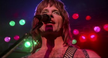 Movie still from “This Is Spinal Tap” (1984), directed by Rob Reiner – A man with long hair is singing into a microphone; Close Up shot, Low angle