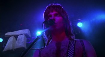Movie still from “This Is Spinal Tap” (1984), directed by Rob Reiner – A man with long hair is singing into a microphone; Close Up shot, Low angle