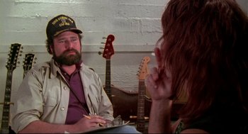 Movie still from “This Is Spinal Tap” (1984), directed by Rob Reiner – A man and a woman sitting next to each other in front of guitars; Close Up shot, Over the shoulder angle