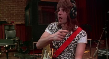 Movie still from “This Is Spinal Tap” (1984), directed by Rob Reiner – A man wearing headphones and holding a guitar; Medium shot, Low angle