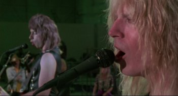 Movie still from “This Is Spinal Tap” (1984), directed by Rob Reiner – A man with a microphone in his mouth performing; Close Up shot, Low angle