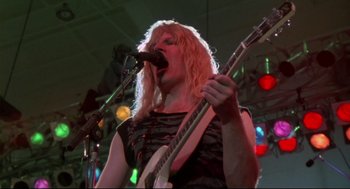 Movie still from “This Is Spinal Tap” (1984), directed by Rob Reiner – A man with long blonde hair is holding a guitar; Medium shot, Low angle