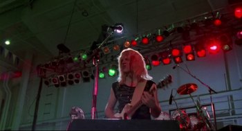Movie still from “This Is Spinal Tap” (1984), directed by Rob Reiner – A woman playing a guitar in front of an audience; Medium shot, Low angle