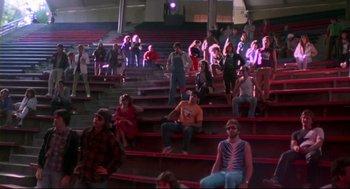 Movie still from “This Is Spinal Tap” (1984), directed by Rob Reiner – A group of people sitting on top of red seats in an arena; Wide shot, High angle