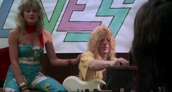 Movie still from “This Is Spinal Tap” (1984), directed by Rob Reiner – A man with blonde curly hair playing an electric guitar; Medium shot, Low angle