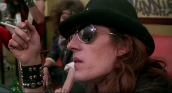 Movie still from “This Is Spinal Tap” (1984), directed by Rob Reiner – A man with a hat and sunglasses is smoking a cigarette; Close Up shot, Low angle