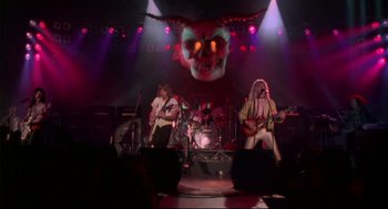 Movie still from “This Is Spinal Tap” (1984), directed by Rob Reiner – A group of people on a stage playing guitar and drums; Wide shot, Low angle