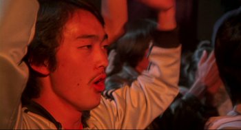 Movie still from “This Is Spinal Tap” (1984), directed by Rob Reiner – A young man is sitting in front of a group of people; Close Up shot, Low angle
