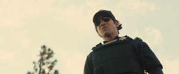 Movie still from “Those Who Wish Me Dead” (2021), directed by Taylor Sheridan – A man in a police uniform with a hat and sunglasses on; Close Up shot, Low angle