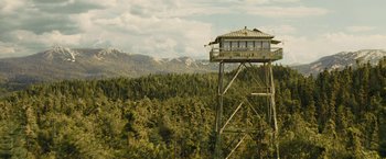 Movie still from “Those Who Wish Me Dead” (2021), directed by Taylor Sheridan – A tall tower with a building on top of it in the middle of a forest; Extreme Wide shot, Low angle