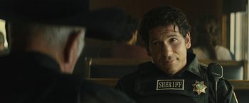 Movie still from “Those Who Wish Me Dead” (2021), directed by Taylor Sheridan – A man wearing a sheriff badge sitting in front of another man; Close Up shot, Over the shoulder angle