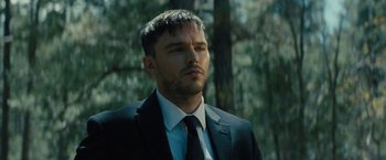 Movie still from “Those Who Wish Me Dead” (2021), directed by Taylor Sheridan – A man wearing a suit and tie standing in front of trees; Close Up shot, Low angle