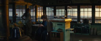 Movie still from “Those Who Wish Me Dead” (2021), directed by Taylor Sheridan – A woman sitting at a table looking at her cell phone; Wide shot, Low angle