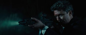 Movie still from “Those Who Wish Me Dead” (2021), directed by Taylor Sheridan – A man in a suit holding a gun in a dark room; Close Up shot, Over the shoulder angle