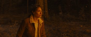 Movie still from “Those Who Wish Me Dead” (2021), directed by Taylor Sheridan – A woman wearing a brown jacket standing in the woods; Medium shot, Over the shoulder angle