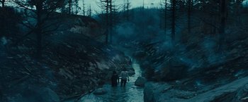 Movie still from “Those Who Wish Me Dead” (2021), directed by Taylor Sheridan – Two people are walking through a stream in the woods; Extreme Wide shot, High angle