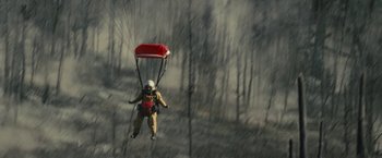 Movie still from “Those Who Wish Me Dead” (2021), directed by Taylor Sheridan – A man is flying a parachute over a forest; Extreme Wide shot, Overhead angle