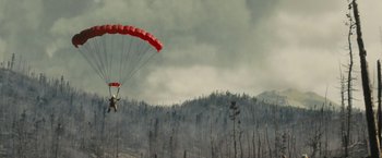 Movie still from “Those Who Wish Me Dead” (2021), directed by Taylor Sheridan – A man is parachuting in the air over a burned forest; Extreme Wide shot, Low angle
