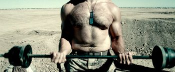 Movie still from “Three Kings” (1999), directed by David O. Russell – A man with a hairy chest holding a stick in the desert; Medium shot, Low angle