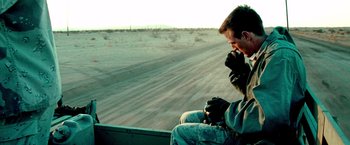 Movie still from “Three Kings” (1999), directed by David O. Russell – A man sitting in a vehicle on the side of a road; Medium shot, Over the shoulder angle